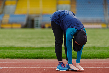 Image showing A Muslim woman in a burqa, an Islamic sports outfit, is doing body exercises, stretching her neck, legs and back after a hard training session on the marathon course.