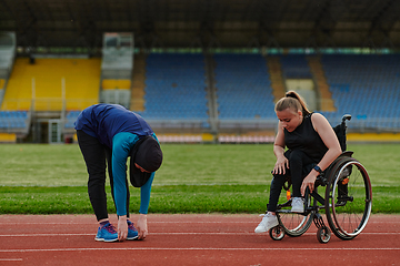 Image showing Two strong and inspiring women, one a Muslim wearing a burka and the other in a wheelchair stretching and preparing their bodies for a marathon race on the track