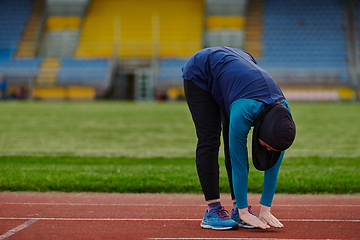 Image showing A Muslim woman in a burqa, an Islamic sports outfit, is doing body exercises, stretching her neck, legs and back after a hard training session on the marathon course.