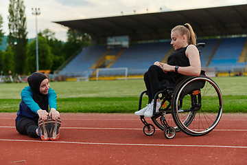 Image showing Two strong and inspiring women, one a Muslim wearing a burka and the other in a wheelchair stretching and preparing their bodies for a marathon race on the track