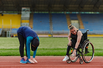 Image showing Two strong and inspiring women, one a Muslim wearing a burka and the other in a wheelchair stretching and preparing their bodies for a marathon race on the track