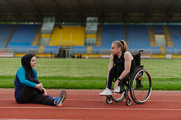 Image showing Two strong and inspiring women, one a Muslim wearing a burka and the other in a wheelchair stretching and preparing their bodies for a marathon race on the track