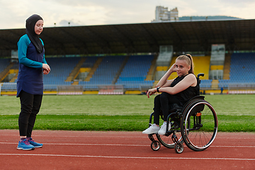 Image showing Two strong and inspiring women, one a Muslim wearing a burka and the other in a wheelchair stretching and preparing their bodies for a marathon race on the track