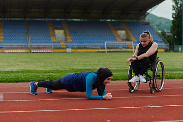 Image showing Two strong and inspiring women, one a Muslim wearing a burka and the other in a wheelchair stretching and preparing their bodies for a marathon race on the track