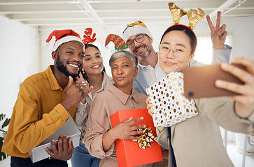 Image showing Business people, Christmas selfie and happy staff with present, peace sign or celebration for diversity at party. Men, women and photography for funny xmas memory, friends or gift for social network