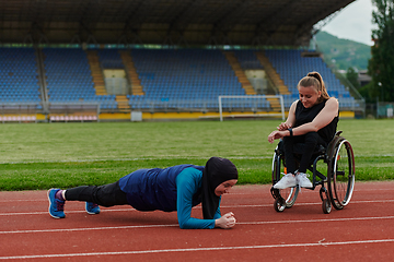 Image showing Two strong and inspiring women, one a Muslim wearing a burka and the other in a wheelchair stretching and preparing their bodies for a marathon race on the track