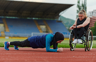 Image showing Two strong and inspiring women, one a Muslim wearing a burka and the other in a wheelchair stretching and preparing their bodies for a marathon race on the track