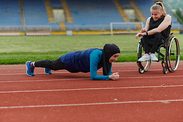 Image showing Two strong and inspiring women, one a Muslim wearing a burka and the other in a wheelchair stretching and preparing their bodies for a marathon race on the track