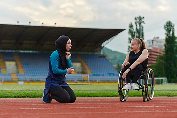 Image showing Two strong and inspiring women, one a Muslim wearing a burka and the other in a wheelchair stretching and preparing their bodies for a marathon race on the track