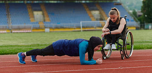 Image showing Two strong and inspiring women, one a Muslim wearing a burka and the other in a wheelchair stretching and preparing their bodies for a marathon race on the track