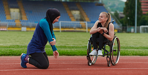 Image showing Two strong and inspiring women, one a Muslim wearing a burka and the other in a wheelchair stretching and preparing their bodies for a marathon race on the track