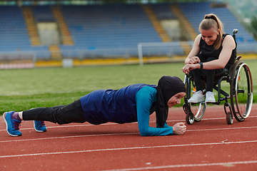 Image showing Two strong and inspiring women, one a Muslim wearing a burka and the other in a wheelchair stretching and preparing their bodies for a marathon race on the track