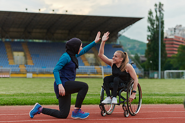 Image showing Two strong and inspiring women, one a Muslim wearing a burka and the other in a wheelchair stretching and preparing their bodies for a marathon race on the track