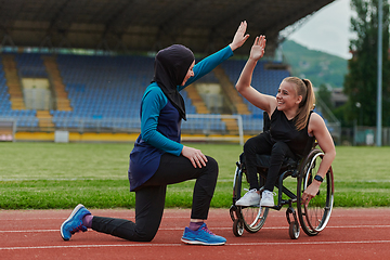 Image showing Two strong and inspiring women, one a Muslim wearing a burka and the other in a wheelchair stretching and preparing their bodies for a marathon race on the track