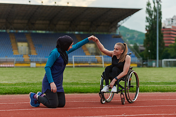 Image showing Two strong and inspiring women, one a Muslim wearing a burka and the other in a wheelchair stretching and preparing their bodies for a marathon race on the track