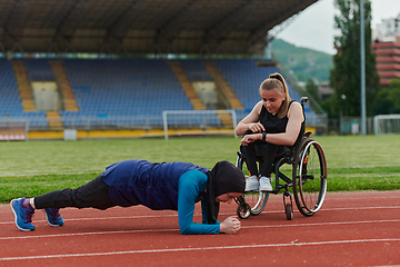 Image showing Two strong and inspiring women, one a Muslim wearing a burka and the other in a wheelchair stretching and preparing their bodies for a marathon race on the track