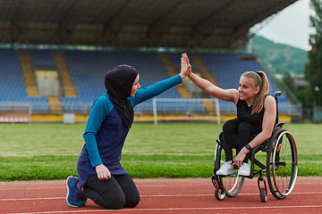 Image showing A Muslim woman wearing a burqa supports her friend with disability in a wheelchair as they train together on a marathon course.