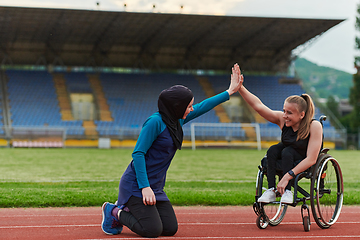 Image showing A Muslim woman wearing a burqa supports her friend with disability in a wheelchair as they train together on a marathon course.