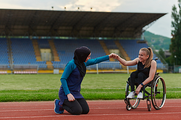 Image showing A Muslim woman wearing a burqa supports her friend with disability in a wheelchair as they train together on a marathon course.