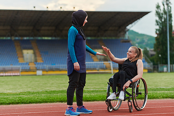 Image showing A Muslim woman wearing a burqa supports her friend with disability in a wheelchair as they train together on a marathon course.