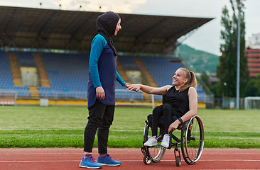 Image showing A Muslim woman wearing a burqa supports her friend with disability in a wheelchair as they train together on a marathon course.