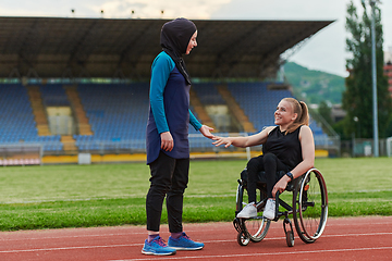 Image showing A Muslim woman wearing a burqa supports her friend with disability in a wheelchair as they train together on a marathon course.