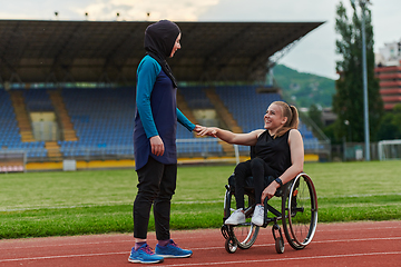 Image showing A Muslim woman wearing a burqa supports her friend with disability in a wheelchair as they train together on a marathon course.