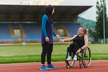 Image showing A Muslim woman wearing a burqa supports her friend with disability in a wheelchair as they train together on a marathon course.