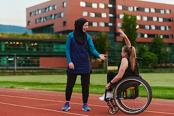 Image showing A Muslim woman wearing a burqa supports her friend with disability in a wheelchair as they train together on a marathon course.