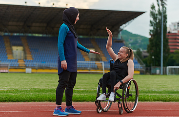 Image showing A Muslim woman wearing a burqa supports her friend with disability in a wheelchair as they train together on a marathon course.