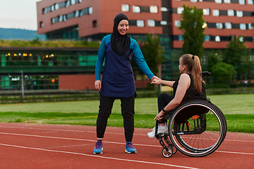 Image showing A Muslim woman wearing a burqa supports her friend with disability in a wheelchair as they train together on a marathon course.