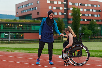 Image showing A Muslim woman wearing a burqa supports her friend with disability in a wheelchair as they train together on a marathon course.