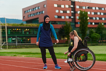 Image showing A Muslim woman wearing a burqa supports her friend with disability in a wheelchair as they train together on a marathon course.