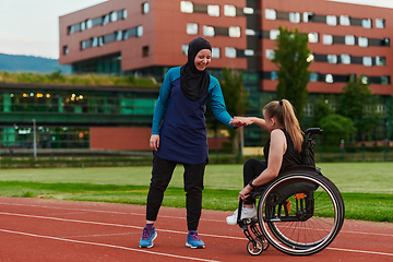 Image showing A Muslim woman wearing a burqa supports her friend with disability in a wheelchair as they train together on a marathon course.