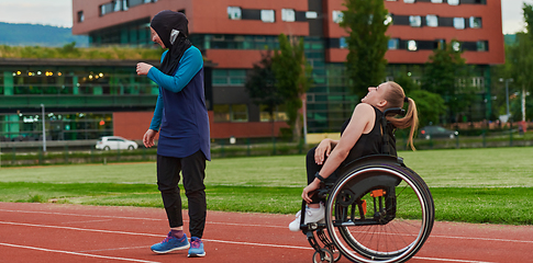 Image showing A Muslim woman wearing a burqa resting with a woman with disability after a hard training session on the marathon course