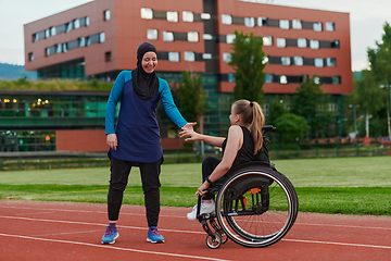 Image showing A Muslim woman wearing a burqa supports her friend with disability in a wheelchair as they train together on a marathon course.