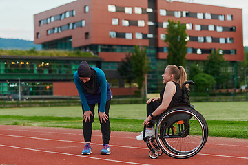 Image showing A Muslim woman wearing a burqa resting with a woman with disability after a hard training session on the marathon course