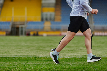 Image showing An inspiring and active elderly couple showcase their dedication to fitness as they running together on a lush green field, captured in a close-up shot of their legs in motion.