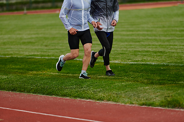 Image showing An inspiring and active elderly couple showcase their dedication to fitness as they running together on a lush green field, captured in a close-up shot of their legs in motion.