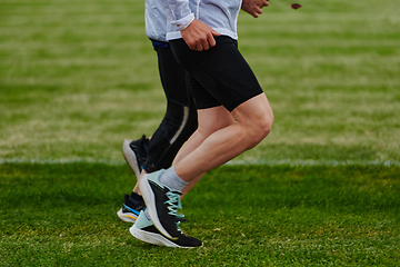 Image showing An inspiring and active elderly couple showcase their dedication to fitness as they running together on a lush green field, captured in a close-up shot of their legs in motion.