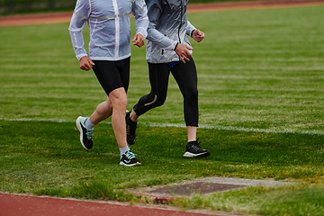 Image showing An inspiring and active elderly couple showcase their dedication to fitness as they running together on a lush green field, captured in a close-up shot of their legs in motion.