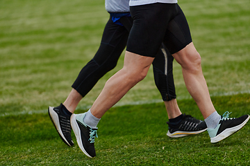 Image showing An inspiring and active elderly couple showcase their dedication to fitness as they running together on a lush green field, captured in a close-up shot of their legs in motion.