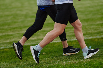 Image showing An inspiring and active elderly couple showcase their dedication to fitness as they running together on a lush green field, captured in a close-up shot of their legs in motion.