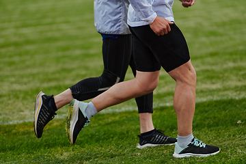 Image showing An inspiring and active elderly couple showcase their dedication to fitness as they running together on a lush green field, captured in a close-up shot of their legs in motion.