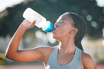 Image showing Drinking water, sports and exercise with a woman outdoor for a run, training or workout. Thirsty African athlete person at stadium for fitness and body wellness with a bottle for hydration and break