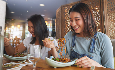 Image showing Restaurant, girl friends and smile with food, noodles and cafe happy from bonding. Asian women, eating and plate together with friendship at a table hungry with chopsticks at Japanese bar gathering