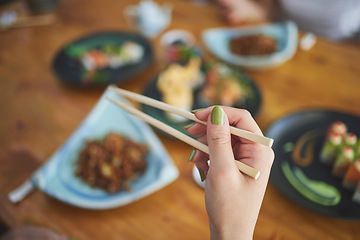 Image showing Chopsticks, hand and a person eating food at a restaurant for nutrition. Closeup of a hungry woman with wooden sticks or utensil for dining, Japanese culture and cuisine on diet with sushi on menu