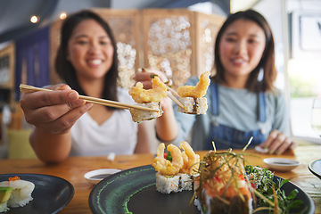 Image showing Chopsticks, girl friends and shrimp sushi at a table with salmon and Japanese cuisine food at restaurant. Young women, eating and tempura prawn with fish for lunch and meal on a plate with a smile