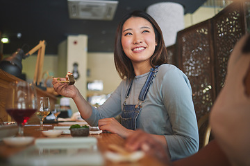 Image showing Asian, sushi and woman at a restaurant eating for dinner or lunch meal using chopsticks and feeling happy with smile. Plate, young and person enjoy Japanese cuisine, noodles or diet at a table