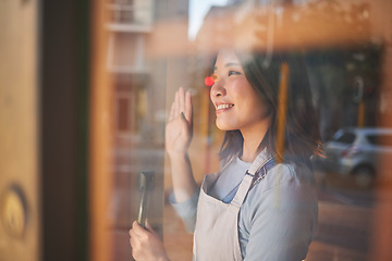 Image showing Asian woman, window and door of restaurant to welcome service, small business owner and wave with reflection. Hello from manager, smile and Japanese food cafe startup with happy entrepreneur at work.